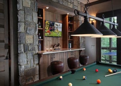 Pool table in a rustic bar room with stone walls, a wooden bar, and hung lights above the cues area.
