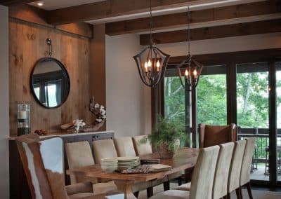 Rustic dining room with a long wooden table, cream chairs, and hanging lantern chandeliers under exposed wooden beams.