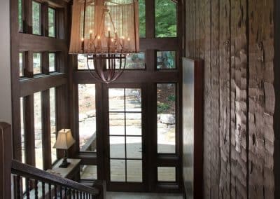 Wood-paneled entry hall with a large chandelier hanging from a vaulted ceiling, view to glass doors and deck outside.