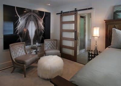 Bedroom seating area with two tufted chairs and a fluffy ottoman, large horse portrait, and a sliding barn door to the bathroom.