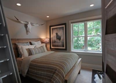 Rustic bedroom with a king bed, wooden headboard, striped bedding, and a longhorn skull mounted above the bed.