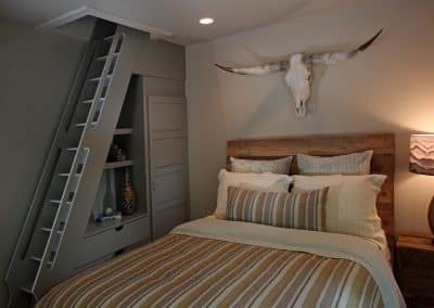 Bedroom with a rustic wooden headboard, striped bedding, and a longhorn skull wall sculpture; built-in storage ladder on the left.