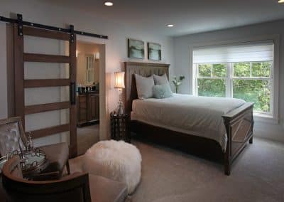 Bedroom with a dark wood bed, sliding barn door, and a large window showing green trees outside.