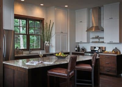Modern kitchen with dark wood island, white cabinets, stainless steel appliances, and a window view of greenery.