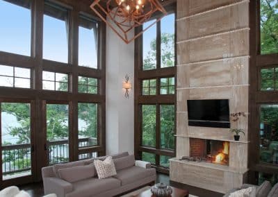 Luxurious living room with tall windows, wooden beams, and a stone fireplace with a TV above it.