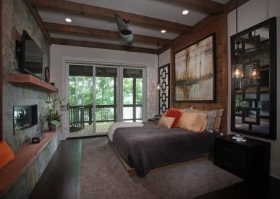 Bedroom with a low platform bed, stone fireplace, and sliding glass doors to a balcony overlooking trees.