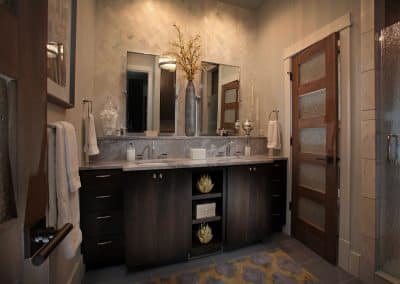 Double-sink bathroom vanity with dark wood cabinets, marble countertop, and two mirrors above it, flanked by towels and decorative items on the counter.